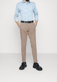 Ljusblå skjorta med lång ärm, i kombination med beige byxor och svarta skor. Svart bälte med flerfärgade detaljer.