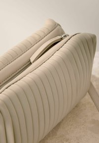 Borsa in pelle beige con cuciture orizzontali, chiusura con zip e superficie testurizzata. Design sottile con tracolla e linee pulite.