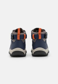 Mėlynos aukštakulnės kedai su pilkais akcentais, oranžinėmis dirželėmis ir tekstūruotais guminiais padu. Yra reguliuojami dirželiai ir paminkštinti apykaklės, užtikrinantys komfortą.