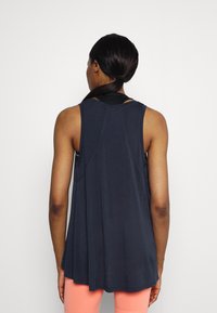 Débardeur de sport sans manches bleu marine à coupe décontractée, avec un ourlet arrondi et des détails de couture subtils, associé à des leggings rose clair.