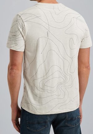 T-shirt beige clair avec des motifs de lignes de contour noires. Manches courtes, col rond et texture lisse. Porté avec un jean bleu.