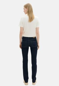 Pantalones vaqueros de mezclilla azul oscuro con un ajuste ajustado, combinados con una camiseta blanca de manga corta. Los vaqueros tienen bolsillos traseros y un diseño minimalista.