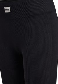 Close-up af sorte ribbet leggings med lille hvid Hummel Performance logo-patch på taljen.