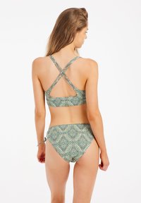 Zestaw bikini z zielonym wzorowanym materiałem w geometryczne wzory. Skrzyżowane ramiączka na górze oraz regulowane zawiązanie z boku dolnej części.