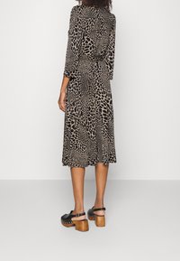 Kleid mit Leopardenmuster in Beige und Schwarz, mit langen Ärmeln, tailliertem Schnitt und einem fließenden Rock. Schwarze Clogs mit Holzabsätzen.