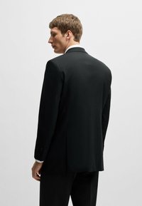 Giacca nera su misura con taglio aderente, spacco singolo sul retro e due bottoni sui polsini. Tessuto liscio, design strutturato.