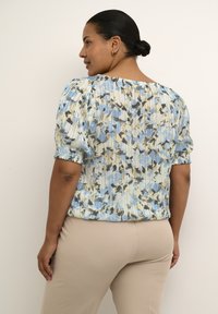 Top con motivo floreale nei toni del blu, crema e grigio; texture plissettata con maniche corte arricciate, caratterizzato da una vestibilità comoda e scollo rotondo.
