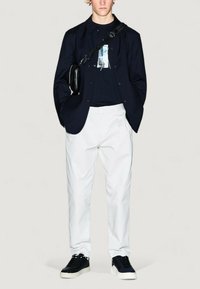 Blazer blu navy su una t-shirt nera con grafica, pantaloni bianchi e sneaker nere. L'outfit include una borsa a tracolla e un design slim fit.