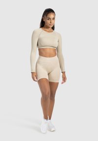 Crop top beige à manches longues et shorts taille haute, fabriqués dans un tissu lisse et extensible, associés à des chaussures de sport blanches.