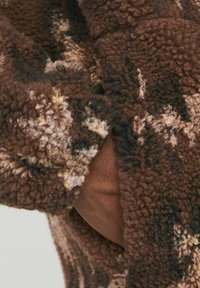 Brown fleece fabric with a textured, fluffy surface featuring a blend of dark and light brown, cream, and black patterns.