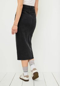 Svart denim midi kjol med en figurnära midja, två bakfickor och subtila sömmar. Bärs med vita sneakers och ribbade grå strumpor.