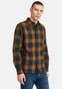Flanellen overhemd in oranje en marineblauw ruitpatroon, met een button-down kraag, lange mouwen en twee voorzakken op de borst.