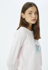 Lichtroze shirt met lange mouwen en een ronde hals, met een bedrukte afbeelding die feestelijke tekst en een gezellige illustratie omvat.