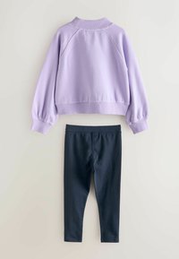 Fialový fleecový pulóver s rebrovaným výstrihom a manžetami, v kombinácii s čiernymi legínami z mäkkého, elastického materiálu. Obe položky sú vystavené na ploche.