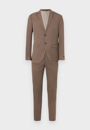 Veste de costume marron à deux boutons avec revers crantés, associée à un pantalon slim assorti, sur un fond blanc uni.