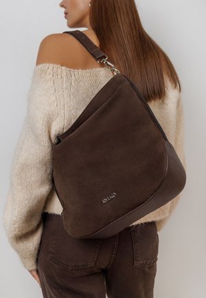 Brown suede shoulder bag with a textured leather bottom, featuring a silver logo detail and an adjustable strap. Wide body design.