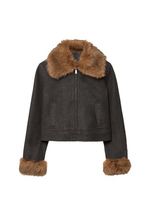 Femme portant une veste courte sombre avec une bordure en fourrure marron au col et aux poignets, associée à un short large taille haute sombre, tenant un sac à main sombre.