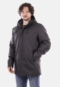 Giacca nera impermeabile con cappuccio, dotata di cordini regolabili, tasche con zip e una finitura testurizzata. Design semplice, con minimi accenti.