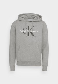 Szara bluza z kapturem wykonana z miękkiego materiału, posiada kieszeń typu kangurka z przodu, ściśnięte mankiety oraz wyraźne logo z stylizowanymi literami "CK."