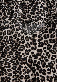 Leopardenmusterstoff mit schwarzen Flecken auf beigem Hintergrund, mit V-Ausschnitt und weichem, strukturiertem Material.