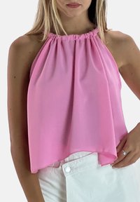 Różowy top na szyję wykonany z lekkiego materiału, z marszczonym dekoltem i luźnym, zwiewnym krojem. Połączony z białymi szortami.