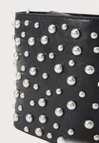 Accessorio in ecopelle nera caratterizzato da borchie metalliche di diverse dimensioni, che creano una superficie testurizzata con un motivo di elementi in rilievo.
