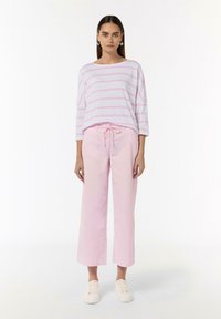 Różowo-biała w paski koszula z długim rękawem w połączeniu z jasnoróżowymi spodniami typu wide-leg. Strój posiada elastyczny pasek w talii i białe sneakersy.