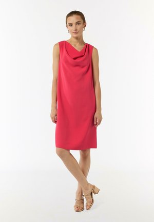 Ärmelloses Kleid mit Stehkragen in leuchtendem Pink, aus glattem Stoff, knielang, kombiniert mit sandfarbenen Blockabsatzsandalen.
