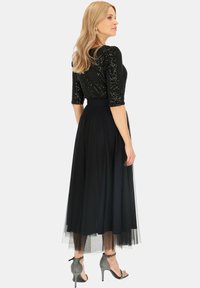 Czarna bluzka z cekinami i rękawami trzyczwartowymi, zestawiona z długą, zwiewną czarną spódnicą z tiulu. Srebrne buty z paskami na kostce dopełniają całość.