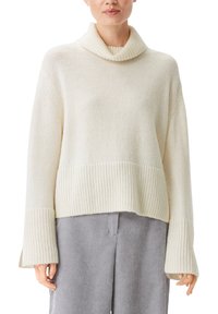 Krämfärgad tröja med grovstickad struktur, uppvikt polokrage och vida ärmar. Har ribbad nederkant och texturerad yta, bärs med randiga byxor.