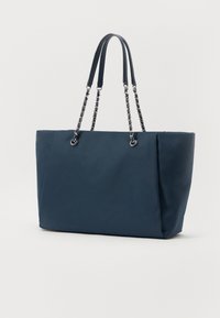 Sac fourre-tout bleu marine en tissu doux, doté de deux poignées et d'accents en chaîne, avec un design spacieux et structuré et une apparence minimaliste.
