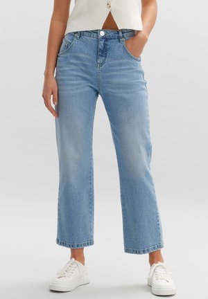 Hellblaue, weit geschnittene Jeans aus Denim, mit hoher Taille, Fronttaschen und rohem Saum. Kombiniert mit weißen Sneakers.