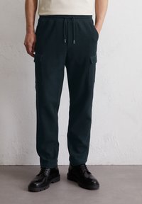 Pantalons cargo vert foncé en tissu doux, avec deux poches latérales, une taille élastique avec un cordon de serrage, et une coupe décontractée.