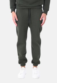 Pantaloni jogger verde scuro realizzati in materiale morbido, con vita elasticizzata e cordoncino, e polsini a costine. Abbinati a sneakers bianche.