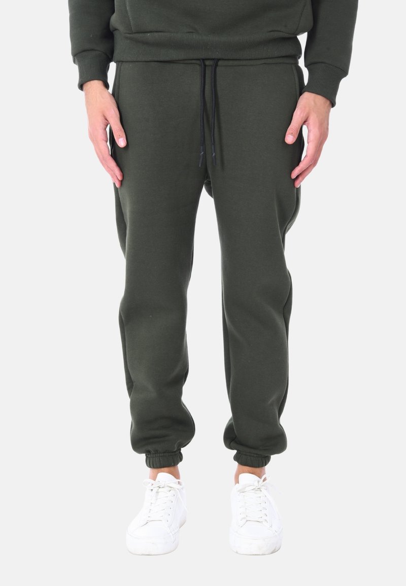 Pantaloni jogger verde scuro realizzati in materiale morbido, con vita elasticizzata e cordoncino, e polsini a costine. Abbinati a sneakers bianche.