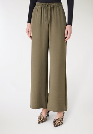 Pantaloni a gamba larga color verde oliva con finitura testurizzata e vita elastica, abbinati a tacchi a punta con stampa leopardata.