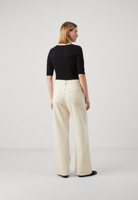 Svart tettsittende topp med korte ermer, parret med høyt midjebelte, vide off-white bukser. Har synlige baklommer og kontraststing.