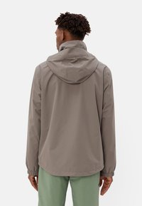 Grijze waterdichte jas voor heren met verstelbare capuchon, elastische manchetten en een gladde textuur, gecombineerd met lichtgroene broek.