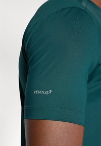 Camisa atlética de manga curta em azul escuro, feita de tecido respirável com uma textura de malha; apresenta um logótipo branco "VENTUS" na manga.