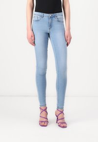 Pantalones vaqueros ajustados de color azul claro con cintura media, cuatro bolsillos y un leve desvanecimiento, combinados con sandalias de tacón alto moradas con tiras.