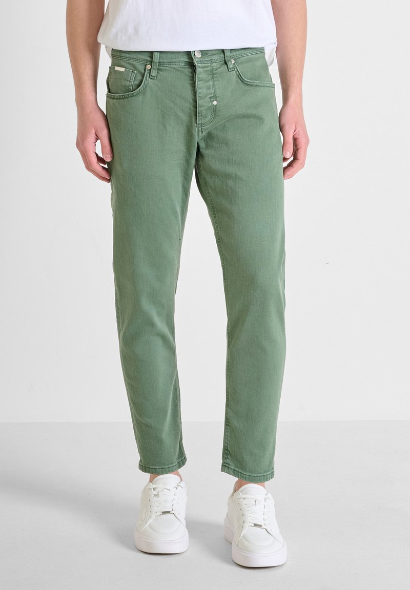 Pantalones de mezclilla verdes con un corte slim, diseño de cinco bolsillos y detalles de costura sutiles. Combinados con zapatillas blancas y una camisa blanca sencilla.