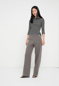 Pasiasty czarno-biały top z długim rękawem i dekoltem w łódkę, w połączeniu z szarymi spodniami o szerokich nogawkach, charakteryzującymi się gładką fakturą i minimalnym zdobieniem.