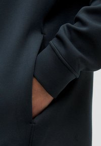 Sudadera gris oscuro con una textura suave, puños acanalados y un bolsillo lateral con un detalle de costura.