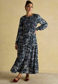 Dlhé rukávy, námornícky šaty s bielou kvetinovou potlačou, smockovaný živôtik a vrstvená sukňa. Spárované s burgundskými balerínami s popruhmi.