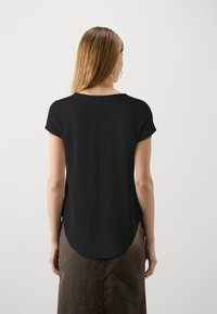 Black short-sleeve top with a scooped neckline and a longer back hem, made of lightweight material; worn with a brown skirt.
