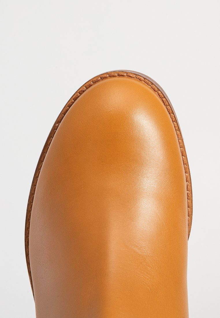 Tan leren enkelboot met een ronde neus, een gladde textuur en contrasterende gestikte afwerking langs de zool.