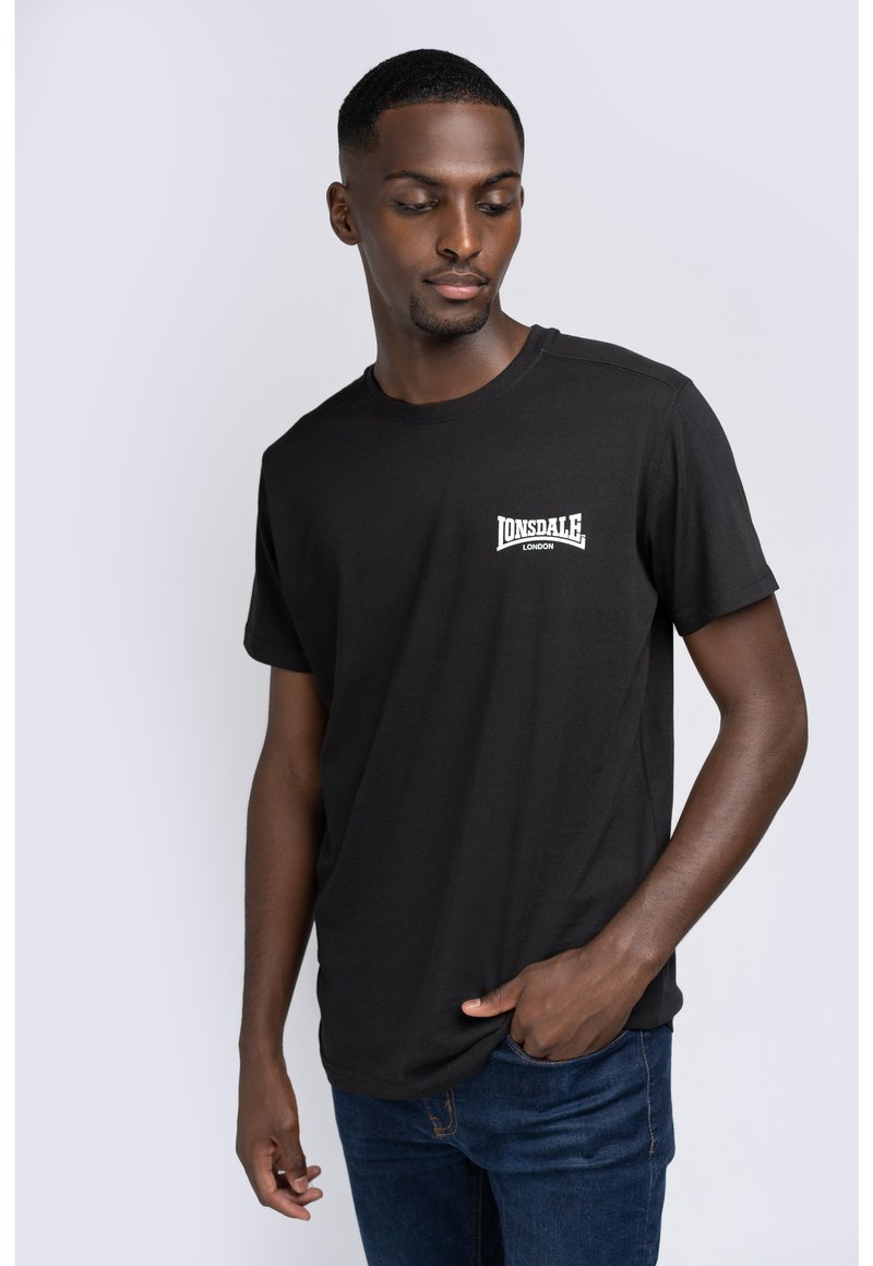 Sort bomulds t-shirt med korte ærmer, der har et hvidt "Lonsdale London" logo på venstre bryst. Båret med mørke denim jeans.