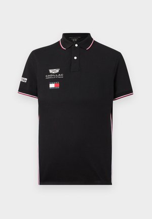 Polo noir avec bordure blanche et rouge, logo de l'équipe Cadillac Formula 1, drapeau Tommy Hilfiger et logo Pirelli sur la manche.