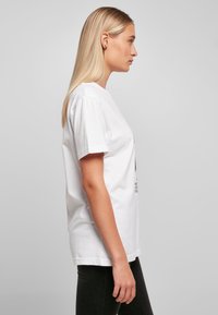 Hvit t-skjorte i bomull med korte ermer, ledig passform. Har trykt design på forsiden og rund hals. Sorte jeans brukt under.