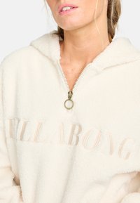 Crème kleurige fleece pullover met een halve rits-kraag, voorzien van een subtiele reliëflogo. Zachte textuur en ontspannen pasvorm, ideaal voor casual wear.